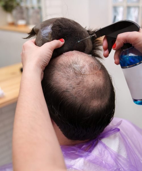 Stylist detaches a hairpiece, starting the maintenance routine.